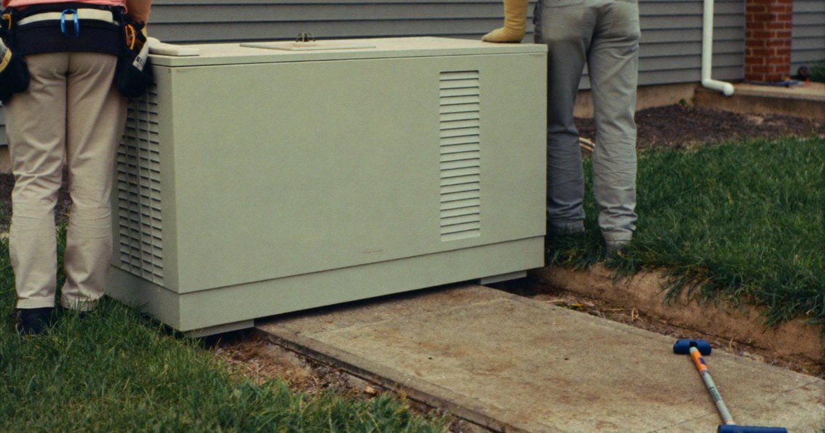 Installers setting a standby generator on a new pad beside a house