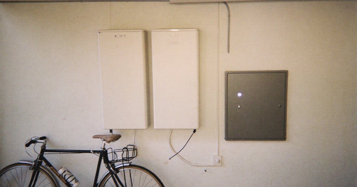Wall-mounted home battery units next to an electrical panel in a garage