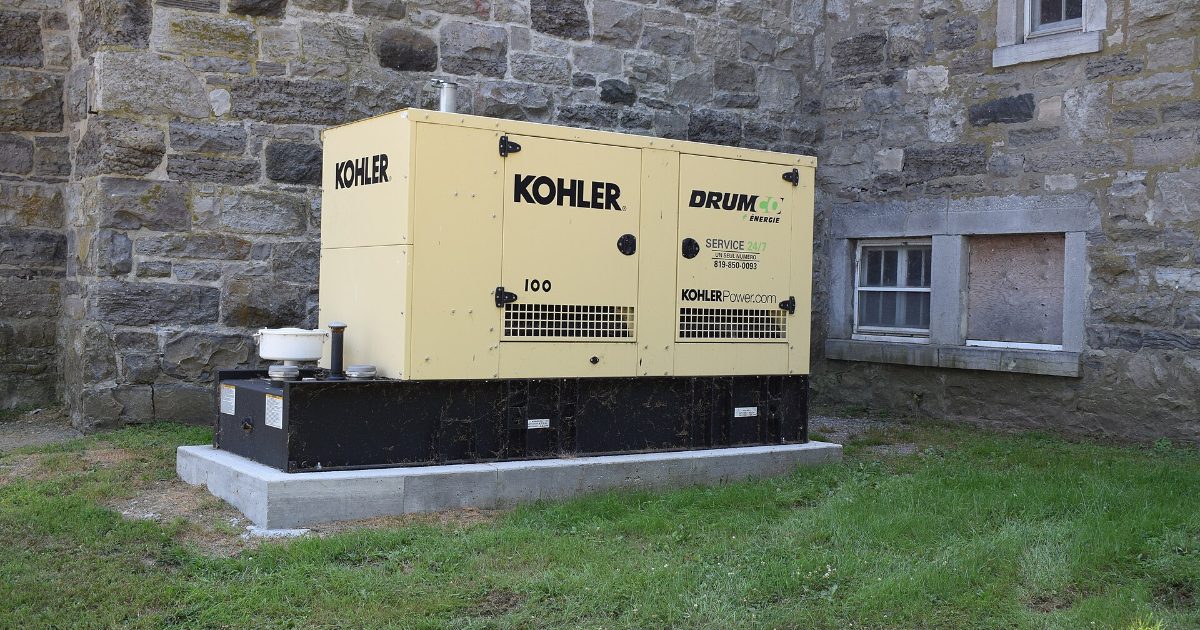 Home standby generator installed on a concrete pad beside a stone house